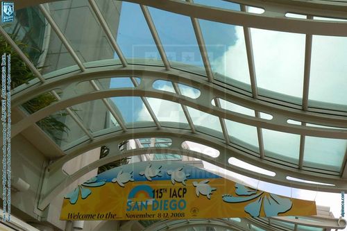 A banner for the 15th IACP conference held in San Diego from November 8-12, 2008, hangs under a modern, glass-paneled ceiling. The banner has a wave design and features seagulls.