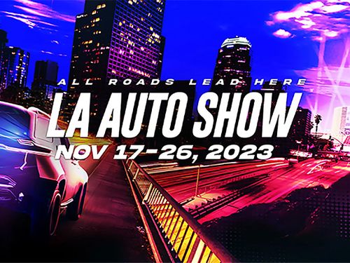 Promotional image for the L.A. Auto Show taking place from November 17 to 26, 2023, featuring city buildings and a car in motion with the tagline "All Roads Lead Here.