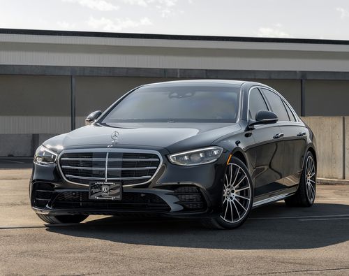 A sleek black, armored Mercedes-Benz S580 4MATIC from Alpine Armoring parked in an outdoor setting. The car features a modern design with a prominent front grille, stylish alloy wheels, and a polished exterior.